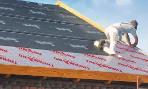 Ocieplenie dachu od zewnątrz. Pracownik montuje izolację THERMANO na konstrukcji dachu.