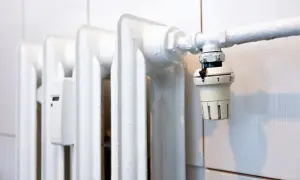 Biały, żeliwny grzejnik z termostatem. Dowiedz się, jak odpowietrzyć grzejnik żeliwny bez odpowietrznika, gdy powietrze blokuje ciepło.