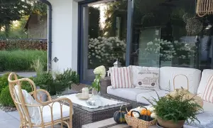 Przytulny taras z rattanowym fotelem i sofą, ozdobiony poduszkami i dyniami. Idealny pomysł na taras galeria dla miłośników relaksu na świeżym powietrzu.