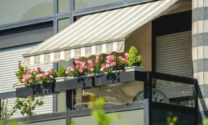 Zadaszenie balkonu bez wiercenia z kwiatami w doniczkach. Pasiasty materiał chroni przed słońcem.