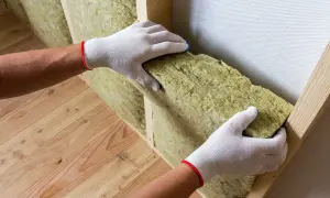 Ręce w białych rękawiczkach montują wełnę mineralną. To dobry sposób, czym ocieplić ściany od wewnątrz, by było ciepło i cicho.