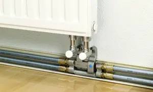 Estetyczne podłączenie grzejnika od dołu z wykorzystaniem systemu PEX. Dwa rury grzewcze, zawory i złączki tworzą schludny system.