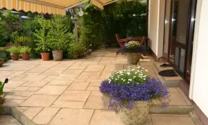 Piękny taras na gruncie z kwitnącymi donicami i zielenią. Idealne miejsce na relaks.