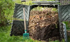Kompostownik pełen resztek organicznych, obok widły. Poznaj sposoby, jak przyspieszyć kompostowanie i uzyskać cenny nawóz.