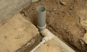 Instalacja kanalizacyjna w domu w trakcie budowy. Szare rury PVC połączone w wykopie ziemnym.