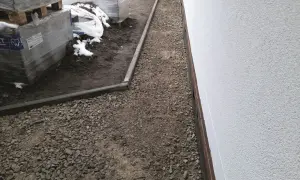 Wykonano opaskę wokół domu z płyt chodnikowych, otaczającą żwirowany teren budowy z paletami kostki brukowej.