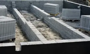 Budowa fundamentów z bloczków betonowych, przygotowanie pod prawidłową izolację fundamentów. Materiały budowlane czekają na użycie.