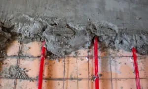 Czerwone rury ogrzewania podłogowego częściowo przykryte mokrą wylewką. Trwa praca nad tym, jaka wylewka na ogrzewanie podłogowe będzie najlepsza.