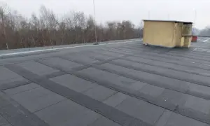 Płaski dach pokryty papą, z widocznym budynkiem technicznym. Szukasz alternatywy co zamiast papy na dach płaski?