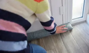 Osoba w kolorowym swetrze układa podkładkę pod drzwi, by jak ocieplić drzwi wejściowe.