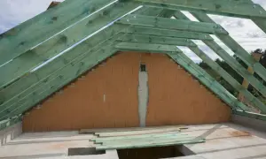 Widok na styk ściany szczytowej z dachem. Drewniana konstrukcja dachu w zielonej impregnacji, ceglana ściana szczytowa.