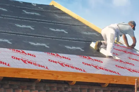 Ocieplenie dachu od zewnątrz. Pracownik montuje izolację THERMANO na konstrukcji dachu.
