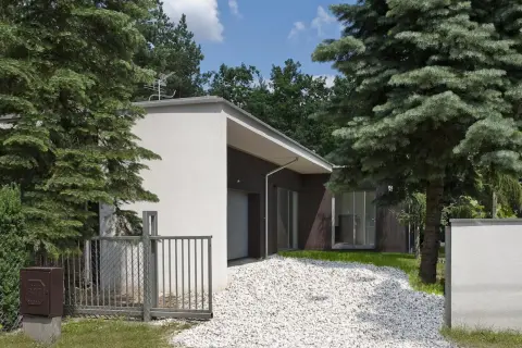Nowoczesny dom z białym podjazdem z kruszywa, otoczony zielenią. Inspiracje dla Twojego ogrodu.