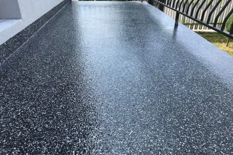 Nowy, błyszczący balkon z żywicą epoksydową w ciemnym kolorze z białymi płatkami. Wygląda nowocześnie i jest łatwy w utrzymaniu.
