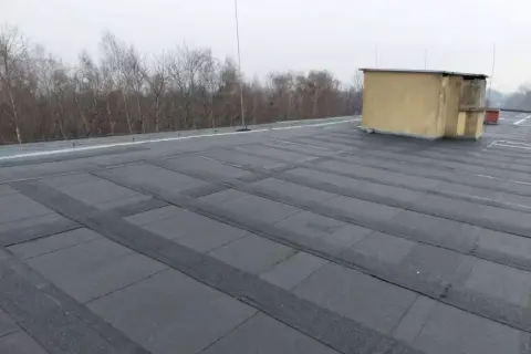 Płaski dach pokryty papą, z widocznym budynkiem technicznym. Szukasz alternatywy co zamiast papy na dach płaski?