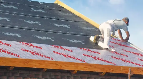 Ocieplenie dachu od zewnątrz. Pracownik montuje izolację THERMANO na konstrukcji dachu.