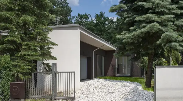 Nowoczesny dom z białym podjazdem z kruszywa, otoczony zielenią. Inspiracje dla Twojego ogrodu.