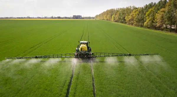 Traktor opryskuje zielone pole, rozpylając płyn. To nie jest adblue na trawnik, lecz środek ochrony roślin.