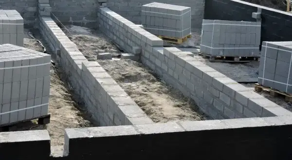 Budowa fundamentów z bloczków betonowych, przygotowanie pod prawidłową izolację fundamentów. Materiały budowlane czekają na użycie.