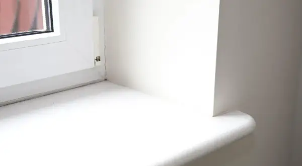 Biały, nowy parapet wewnętrzny po wymianie, z zaokrąglonym rogiem, gotowy na nowe dekoracje.