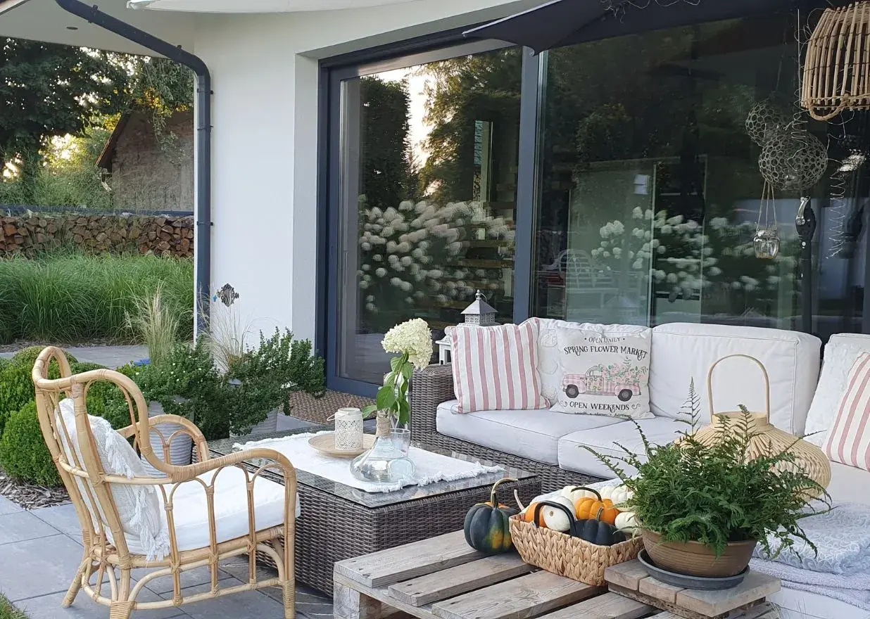 Przytulny taras z rattanowym fotelem i sofą, ozdobiony poduszkami i dyniami. Idealny pomysł na taras galeria dla miłośników relaksu na świeżym powietrzu.