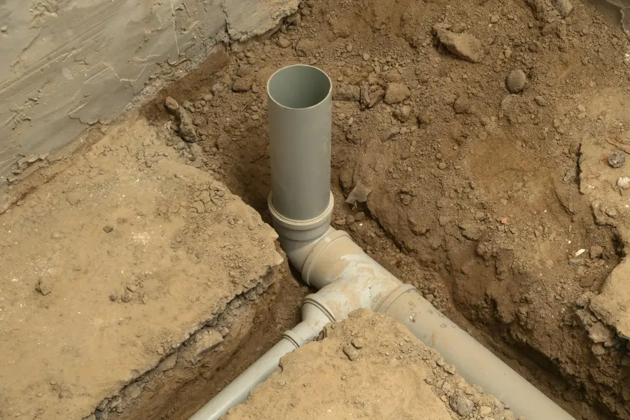 Instalacja kanalizacyjna w domu w trakcie budowy. Szare rury PVC połączone w wykopie ziemnym.