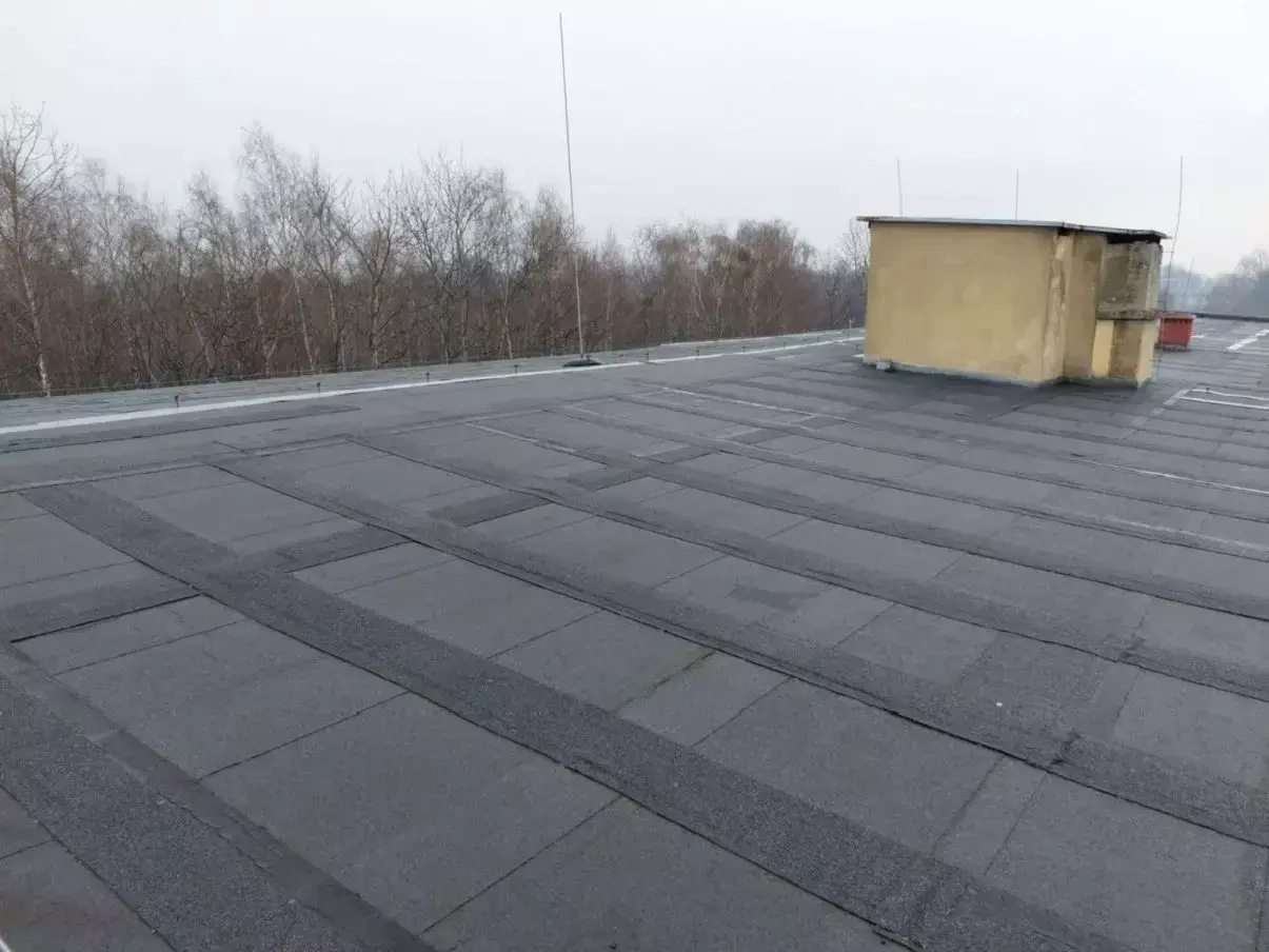 Płaski dach pokryty papą, z widocznym budynkiem technicznym. Szukasz alternatywy co zamiast papy na dach płaski?
