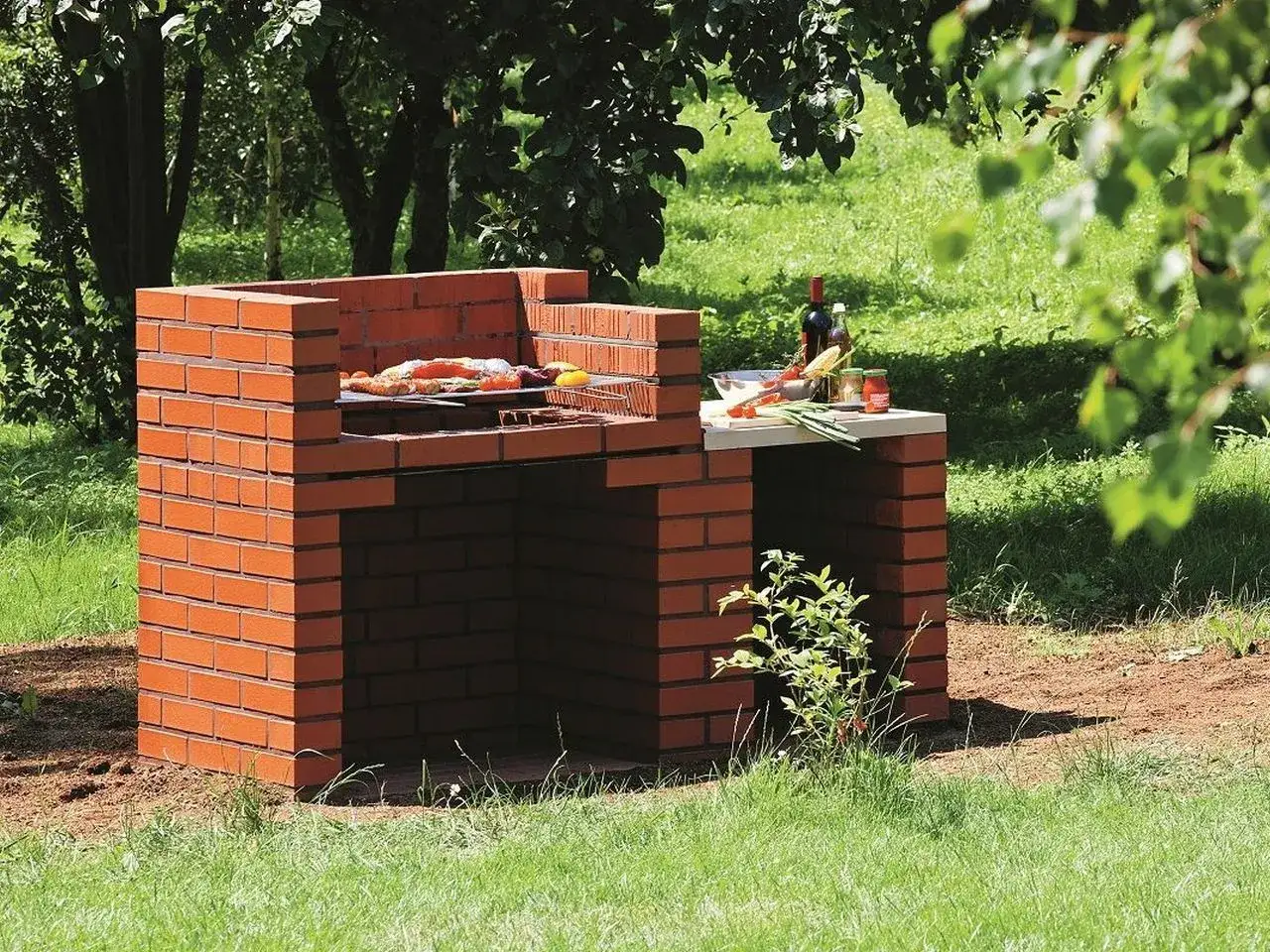 Prosty grill z cegły, gotowy na letnie przyjęcie. Na ruszcie leżą już pierwsze smakołyki, a obok czekają warzywa i butelka wina.
