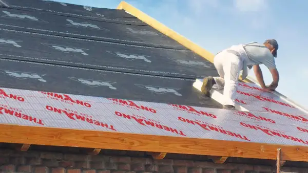 Ocieplenie dachu od zewnątrz. Pracownik montuje izolację THERMANO na konstrukcji dachu.