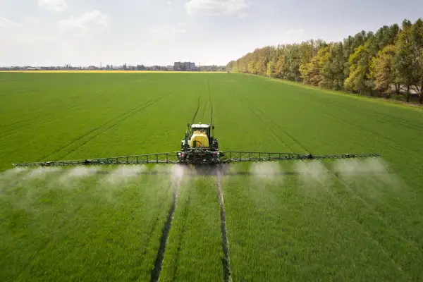 Traktor opryskuje zielone pole, rozpylając płyn. To nie jest adblue na trawnik, lecz środek ochrony roślin.