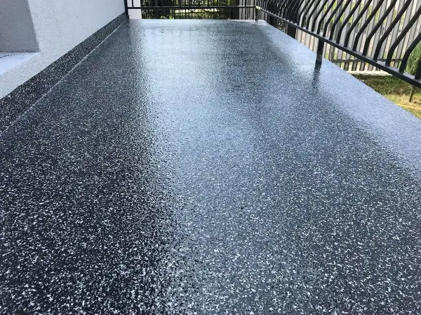 Nowy, błyszczący balkon z żywicą epoksydową w ciemnym kolorze z białymi płatkami. Wygląda nowocześnie i jest łatwy w utrzymaniu.