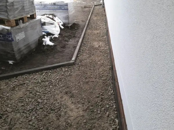 Wykonano opaskę wokół domu z płyt chodnikowych, otaczającą żwirowany teren budowy z paletami kostki brukowej.