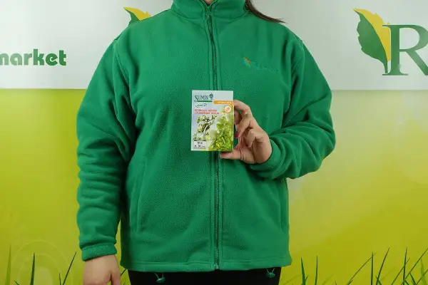 Kobieta w zielonej bluzie trzyma opakowanie stymulatora wzrostu roślin. Na opakowaniu widnieje napis "SUMIN ASAMI SL", a pod nim "STYMULUJE WZROST I PLONOWANIE ROŚLIN". Informacje o dawkowaniu są widoczne na dole.