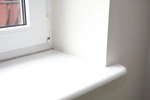 Biały, nowy parapet wewnętrzny po wymianie, z zaokrąglonym rogiem, gotowy na nowe dekoracje.